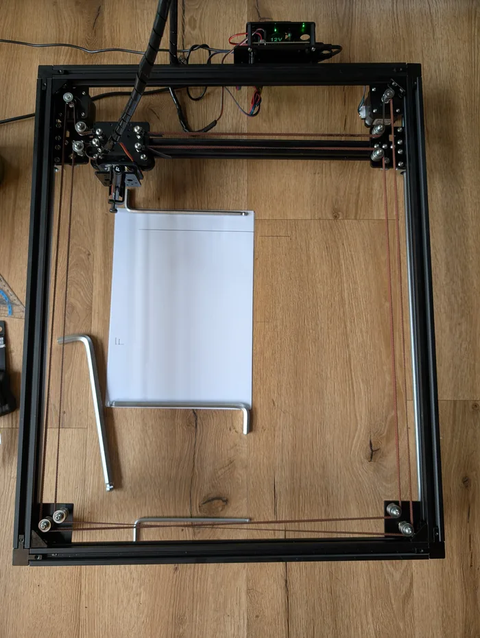Der Plotter von oben: ein rechteckiger Aluprofil-Rahmen mit Riemen, zwei Schrittmotoren und dem Stiftschlitten über einem eingelegten Blatt Papier.